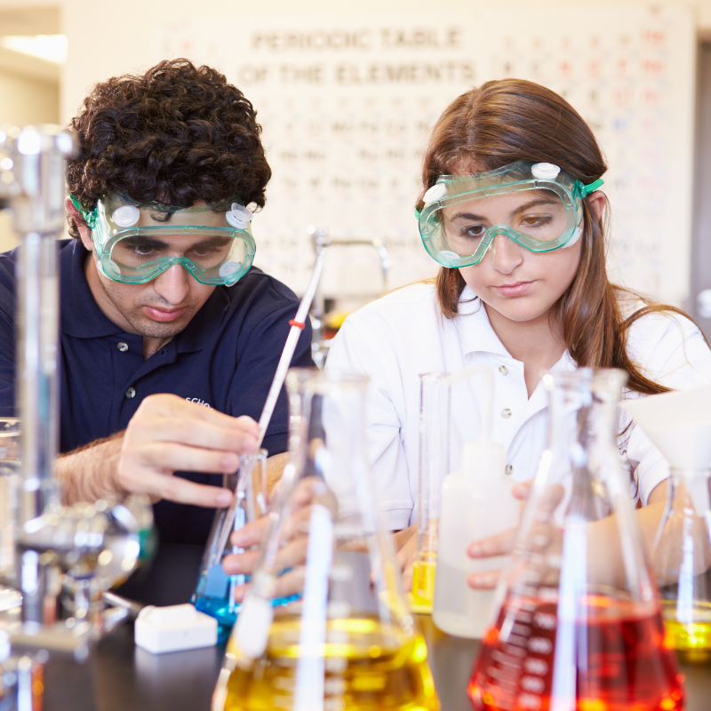 Two students using beakers in a science lab with various colored liquids